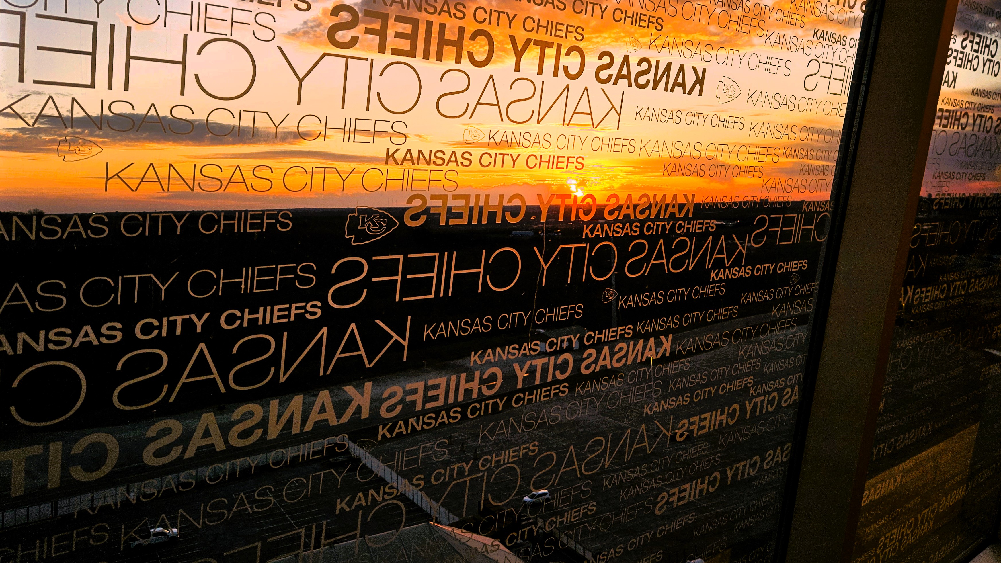 The view from Arrowhead Stadium during sunset, as seen through branded windows featuring the Kansas City Chiefs logo and name.