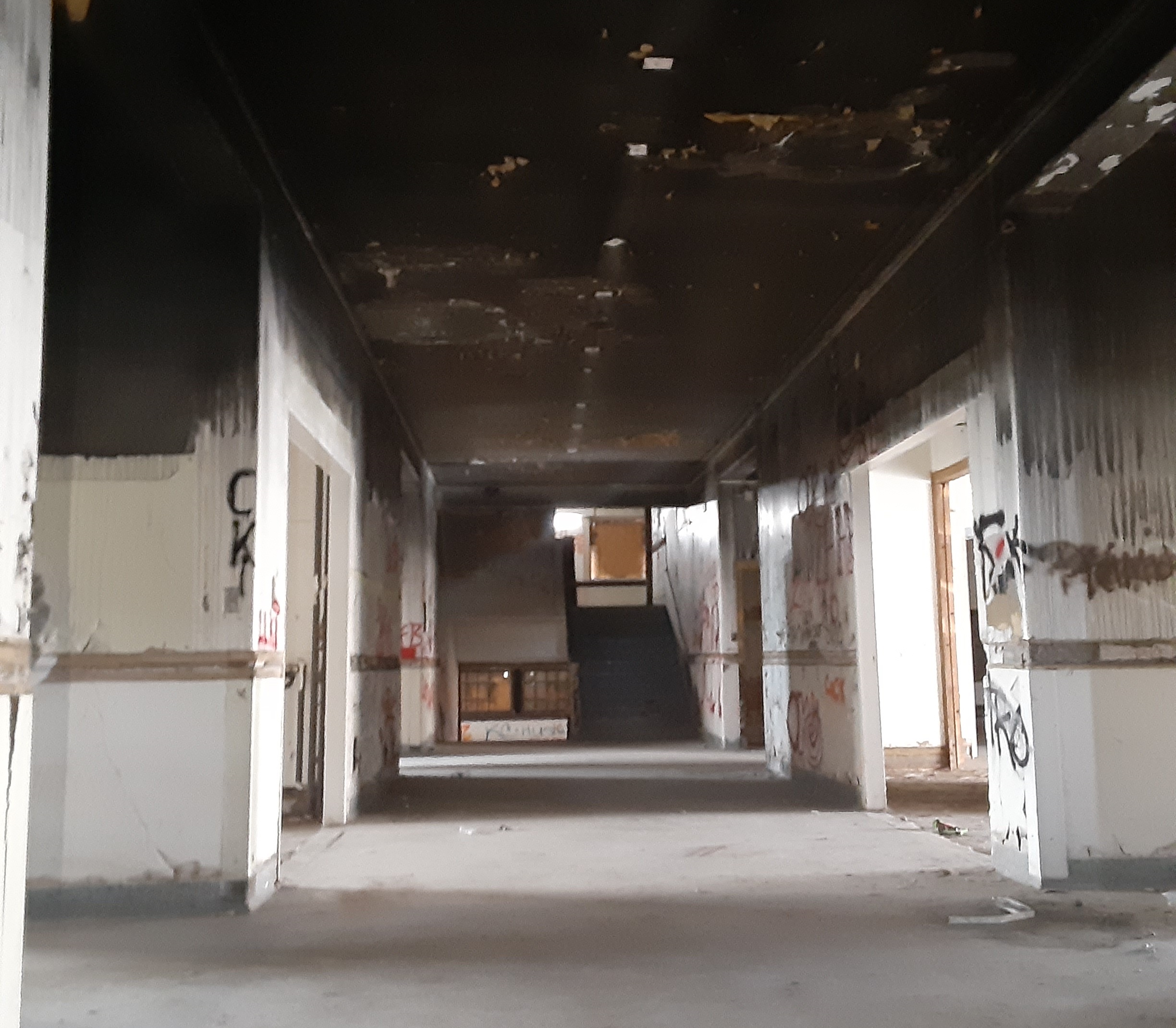 Photo of the 1st floor hallway. There is graffiti visible on a few walls and smoke damage on the ceiling.