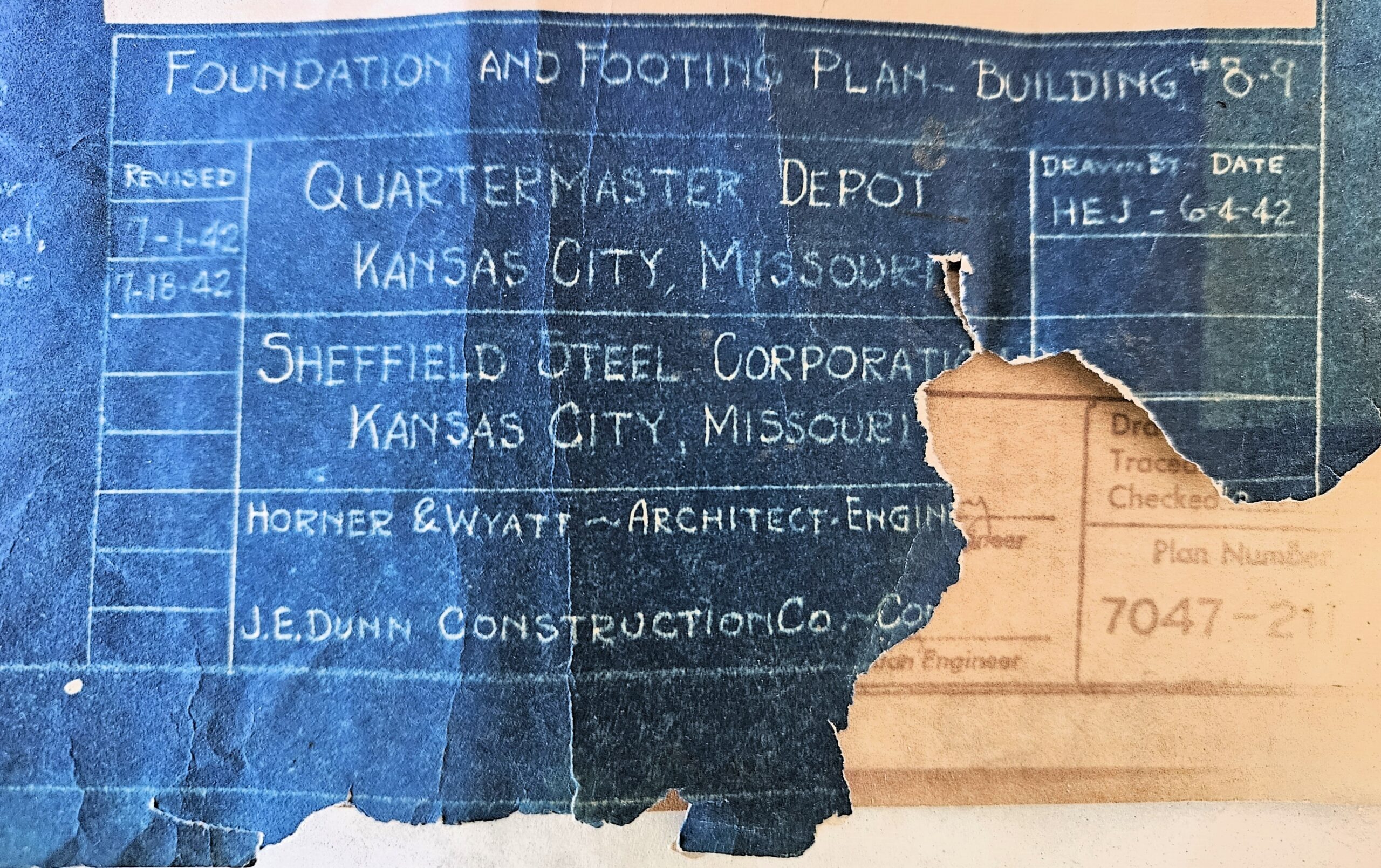 Title block for the one of the foundation blueprints of building 9. It is white print on a dark blue background. The paper is warn and the bottom right corner is missing. It reads "Quartermaster Depot, Kansas City, Missouri" Shefield Steel Corporation, Kansas City, Missouri Horner & Wyatt - Architect Engineer J.E. Dunn Construction Company" The drawing is last dated 7-18-42